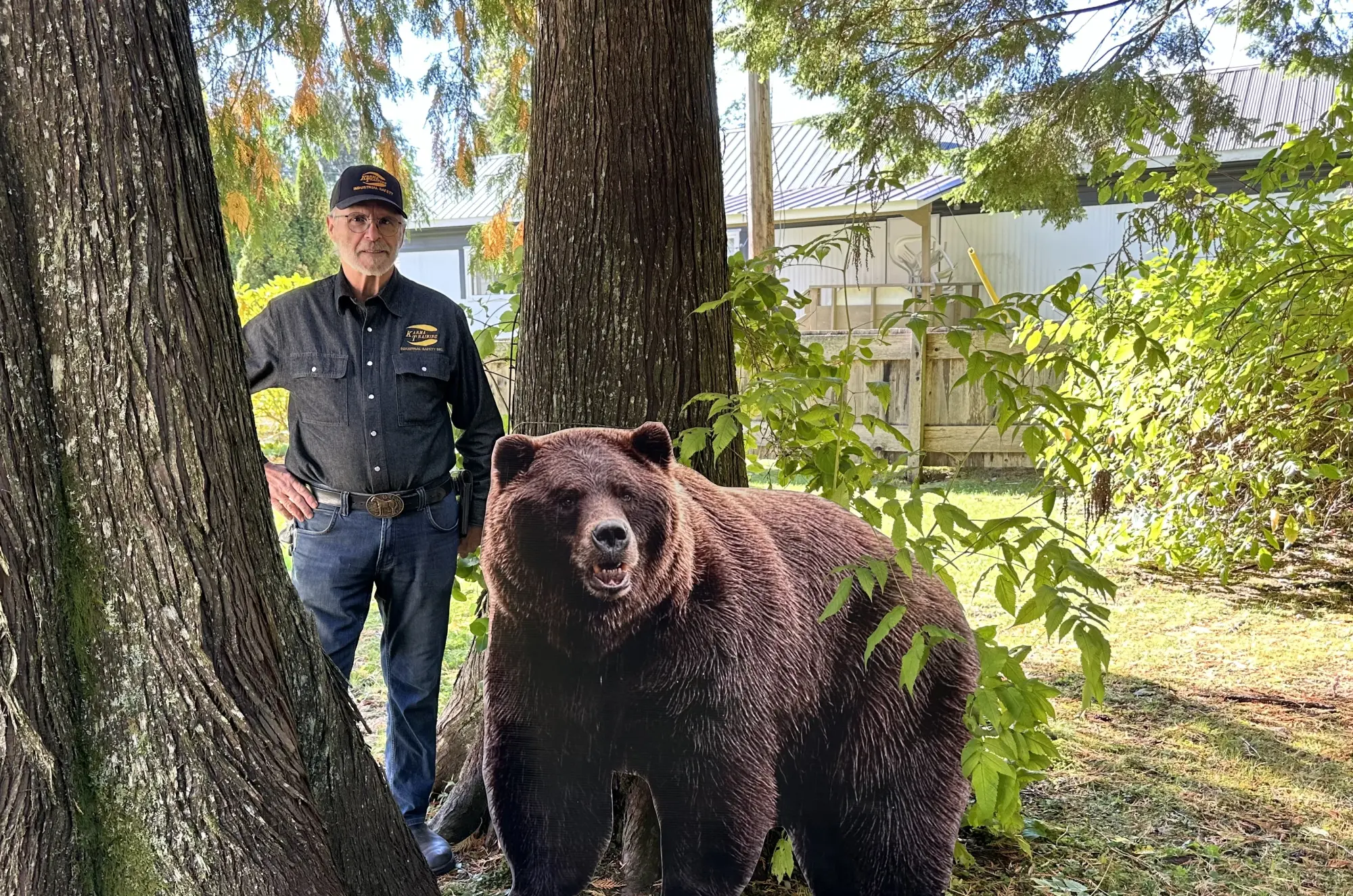 A photograph of Jack Cook, an experienced instructor at Karma Training, a premier safety training provider in Northwestern BC.  He is standing near a large brown bear in a wooded area.
