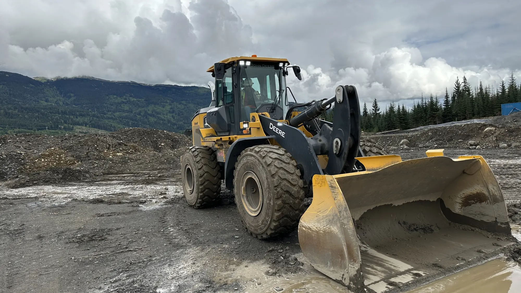 A John Deere wheel loader in a muddy worksite, illustrating hands-on heavy equipment operator training offered by Karma Training in Northwestern BC. The training emphasizes practical skills and adherence to WorkSafeBC regulations.