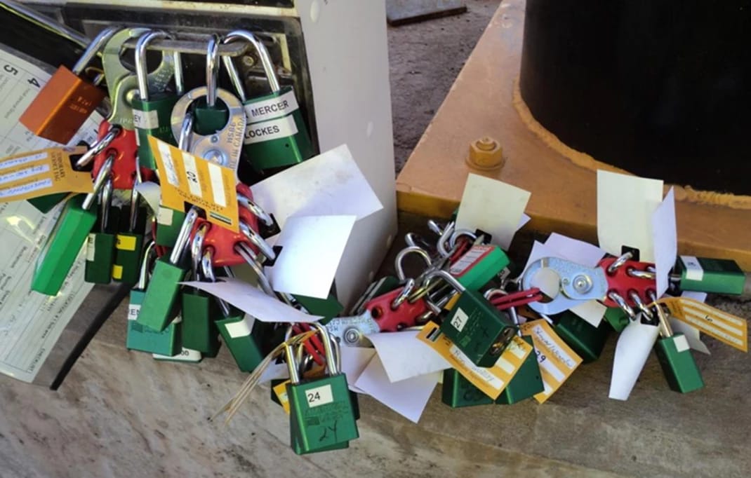 Multiple green and red lockout/tagout LOTO padlocks are secured on a piece of industrial equipment to ensure it is de-energized for maintenance.